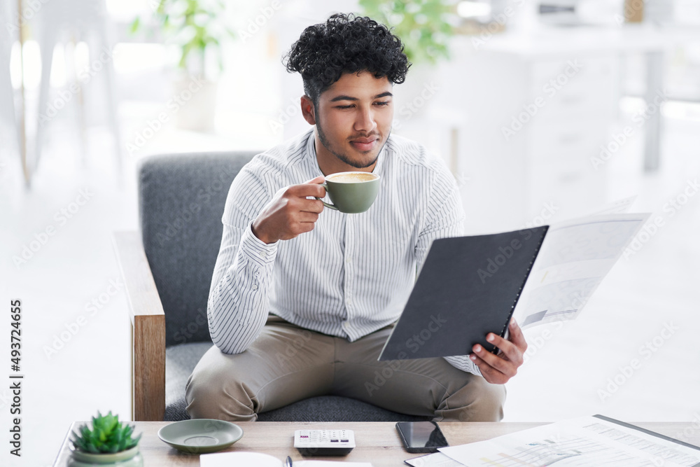 Staying updated with all his paperwork. Shot of a young businessman drinking coffee while going thro