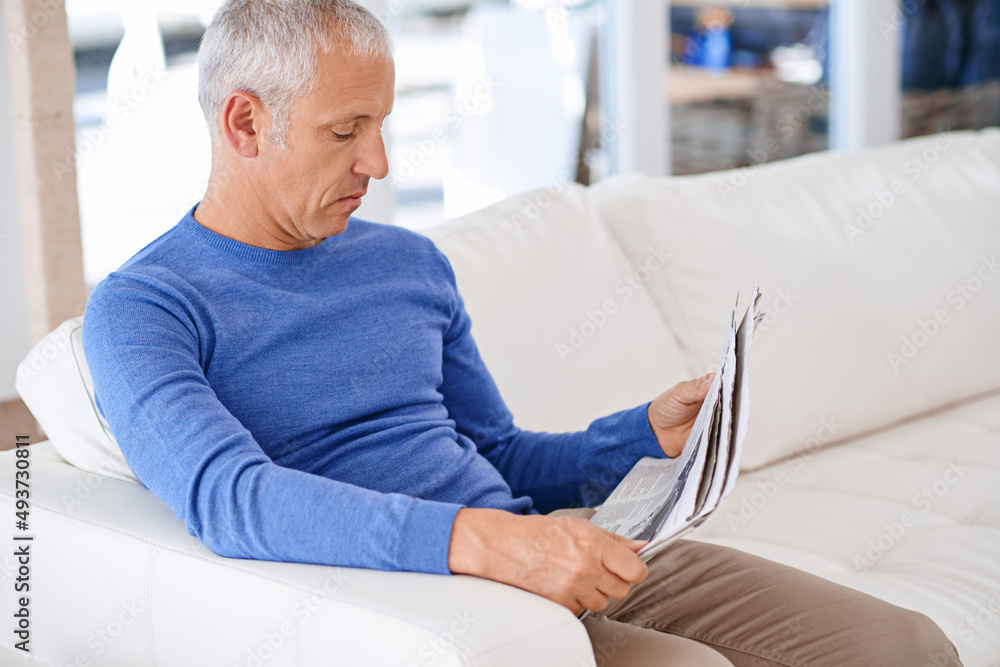 Taking time to catch up on the news. Shot of a mature man sitting on his living room sofa reading a 