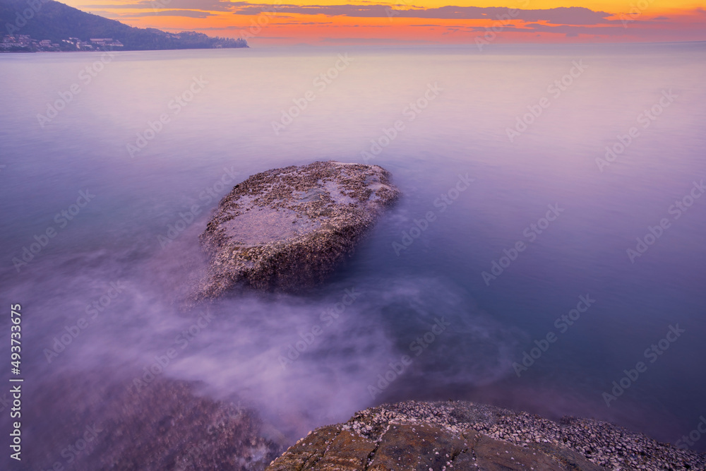 戏剧性的天空海景的长曝光图像，背景是日落或日出时的岩石。