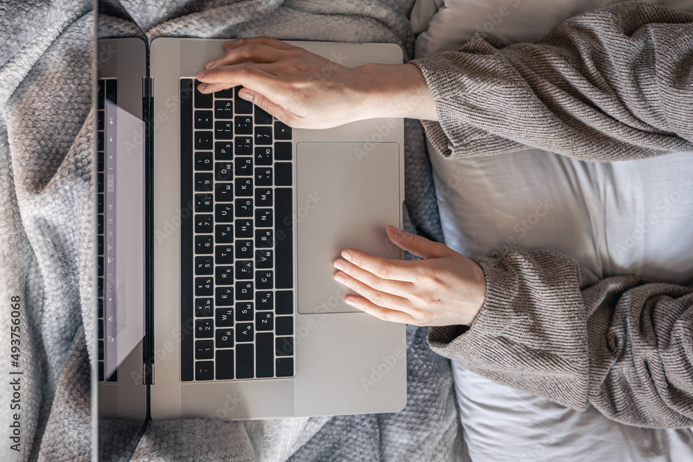 A woman working on a laptop while lying in bed, top view.