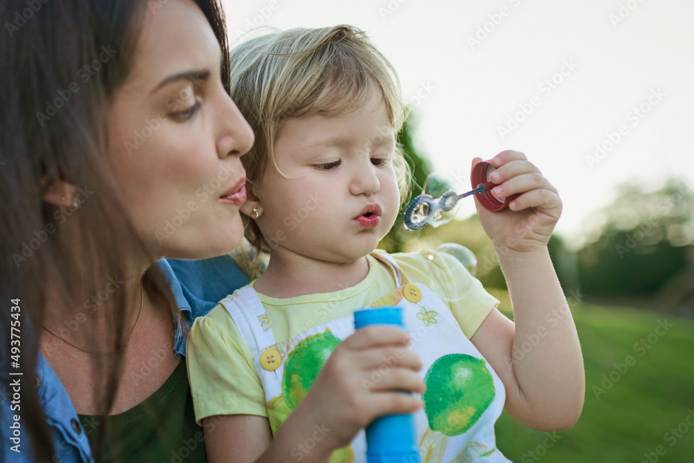 让我们一起吹一个大泡泡。一位母亲和她的小女儿在户外吹泡泡的照片。