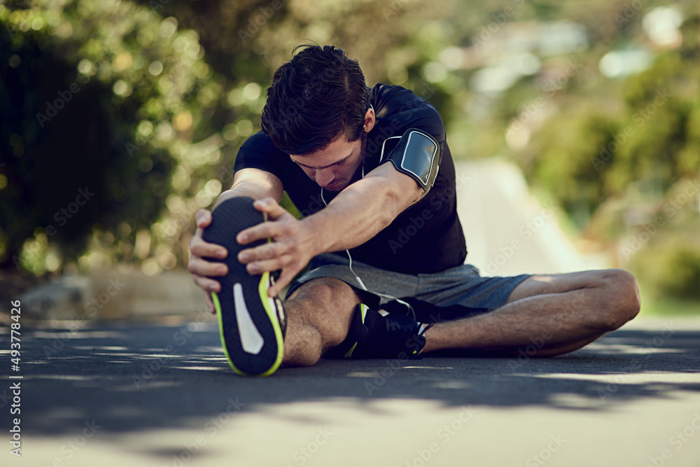 Getting his legs ready for a run. Full length shot of a young man warming up outdoors before a worko