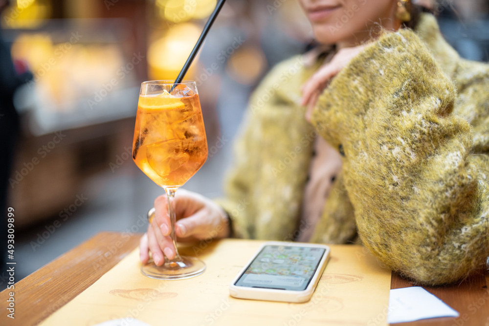 一名女子在户外酒吧拿着装有Aperol雪碧鸡尾酒的杯子，裁剪后的视野聚焦于饮料