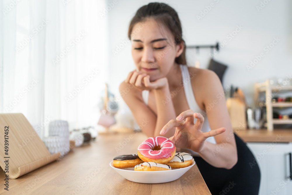 亚洲漂亮的年轻女孩饿了，想在厨房里吃甜甜圈。