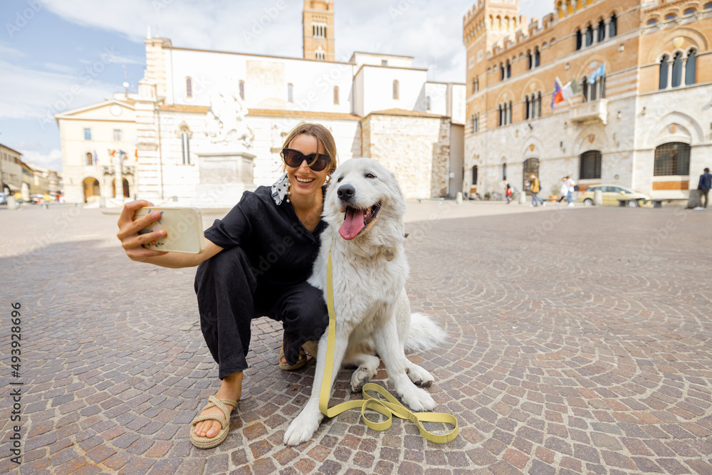 Woman takes selfie photo with dog traveling in Grosseto town the center of Maremma region in Italy. 