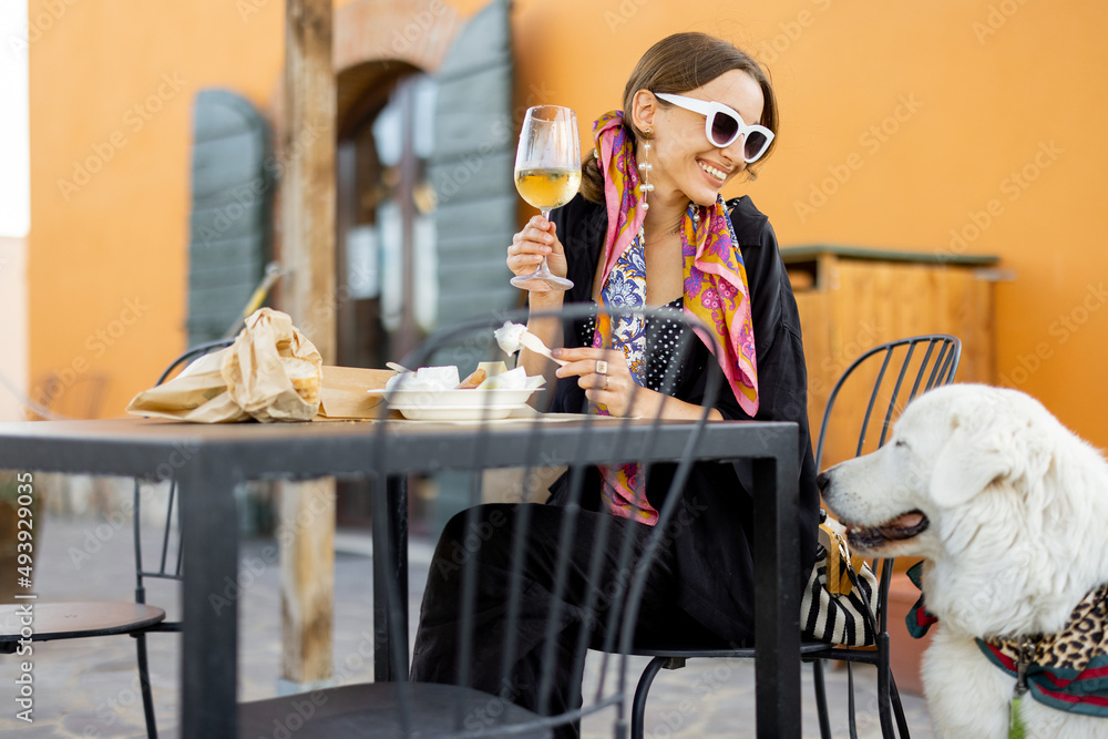 Woman tasting cheese and wine sitting with her dog at local farm shop in Maremma region of Italy. Co