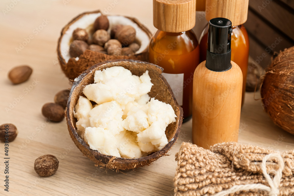 Coconut shell with shea butter an cosmetic products on wooden table, closeup