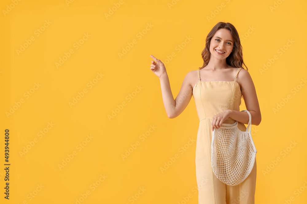 Pretty young woman with string bag pointing at something on yellow background