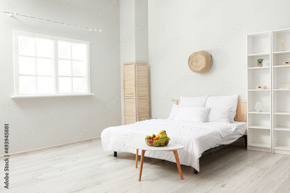 Interior of light bedroom with table and fruit basket