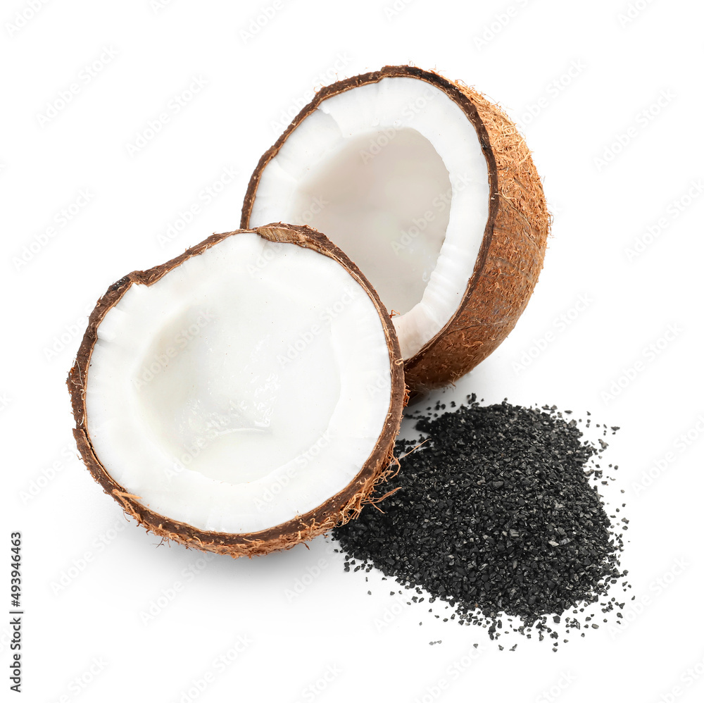 Ripe coconut halves with pile of activated carbon on white background