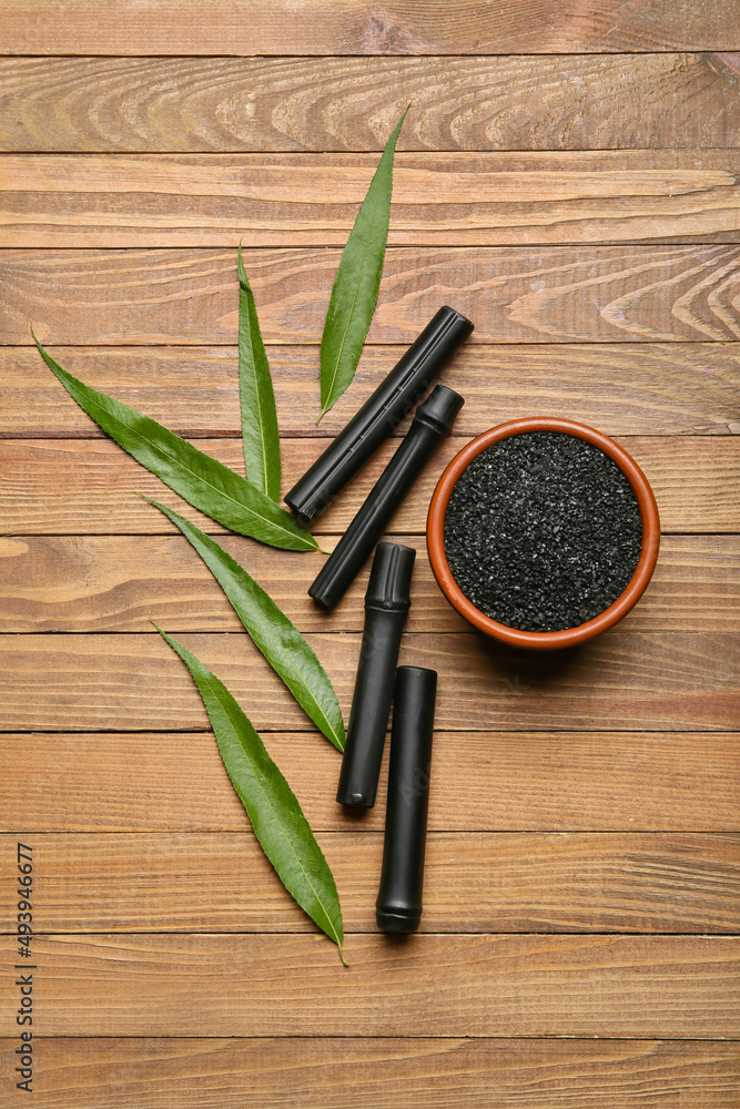 Composition with bowl of activated carbon powder, bamboo sticks and leaves on wooden background