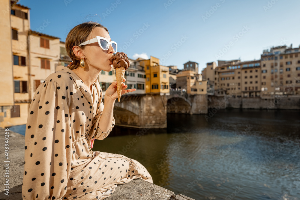 年轻女子坐在河边吃意大利冰淇淋，欣赏著名的奥尔美景