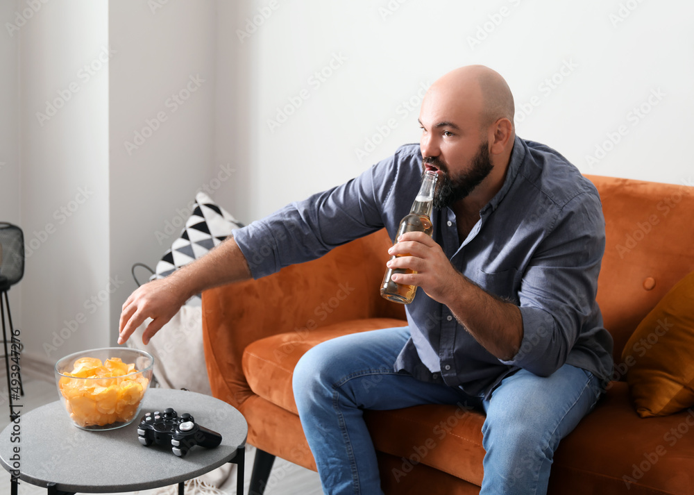 Lazy man drinking beer and eating chips at home