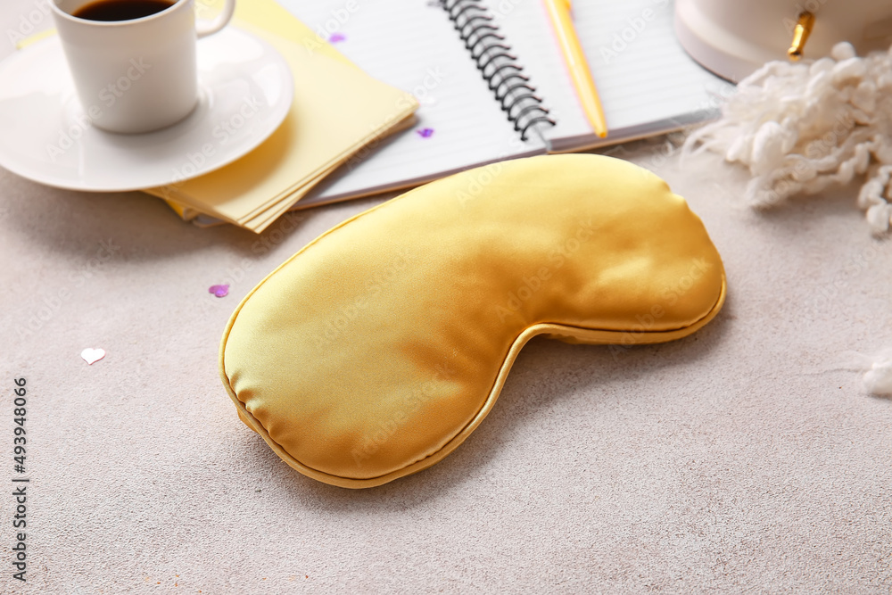 Sleep mask, notebook and cup of coffee on light background