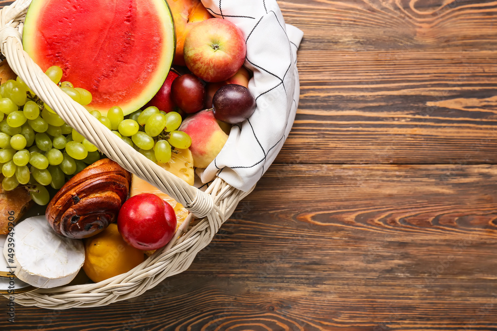 Wicker basket with tasty food for picnic on wooden background