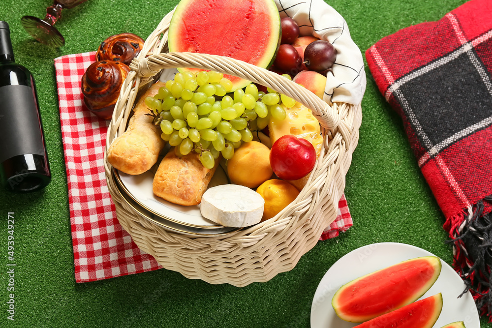 Wicker basket with tasty food for picnic on green background