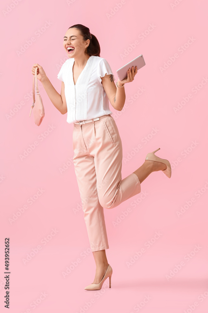 Happy young businesswoman with tablet computer and bag on pink background