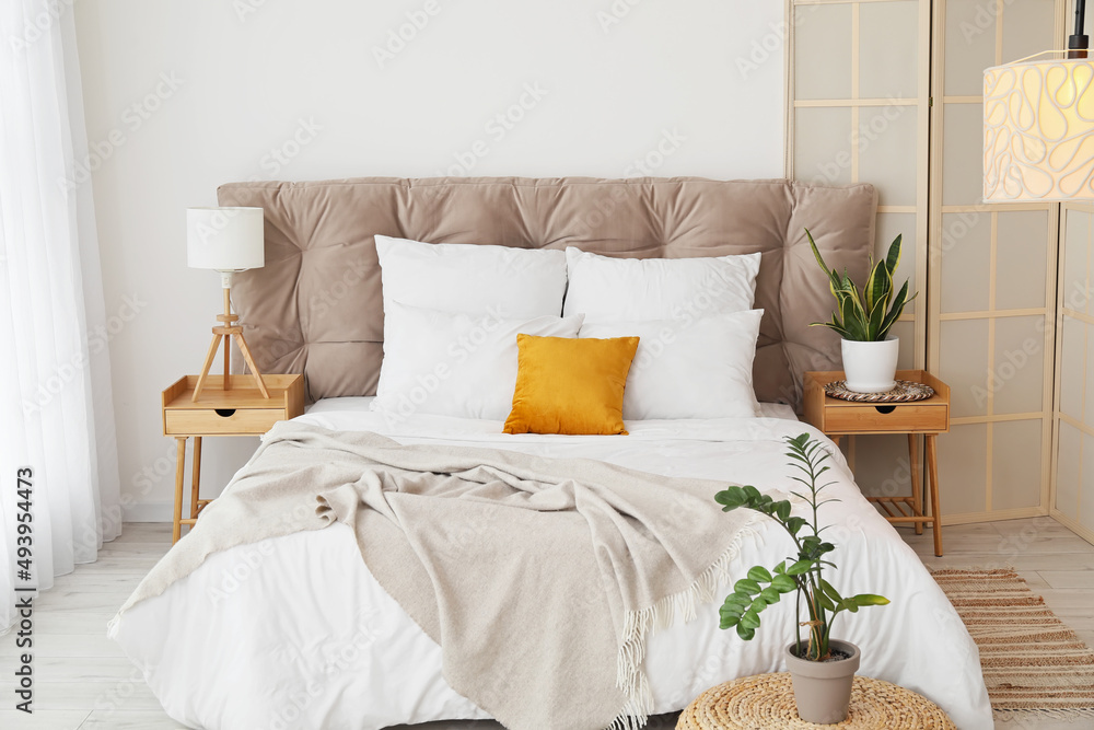 Interior of modern bedroom with stylish folding screen, nightstands and houseplants