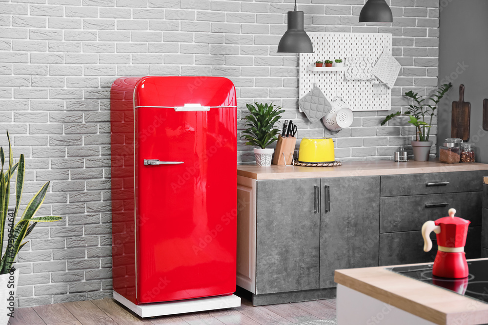 Stylish refrigerator, pegboard, houseplants and counter near grey brick wall in kitchen