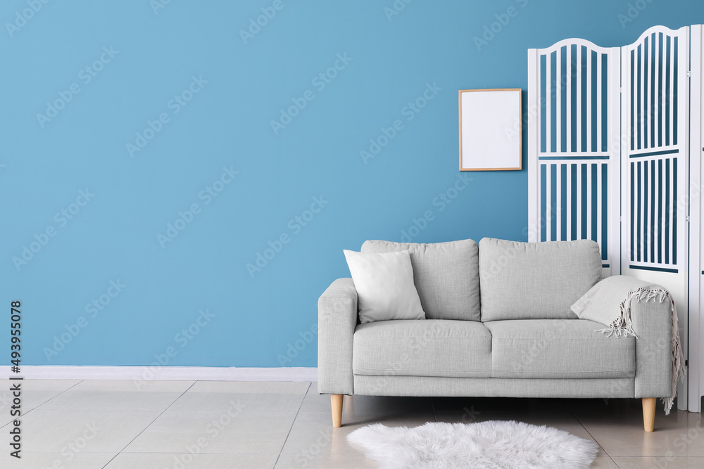 Stylish sofa and folding screen near blue wall