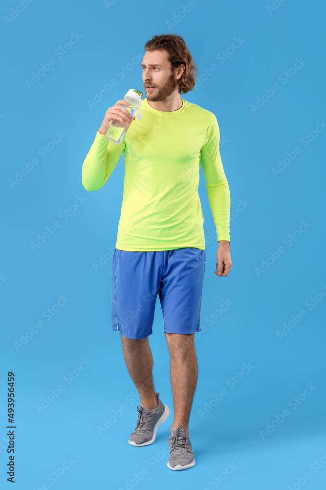 Sporty man with bottle of water on blue background