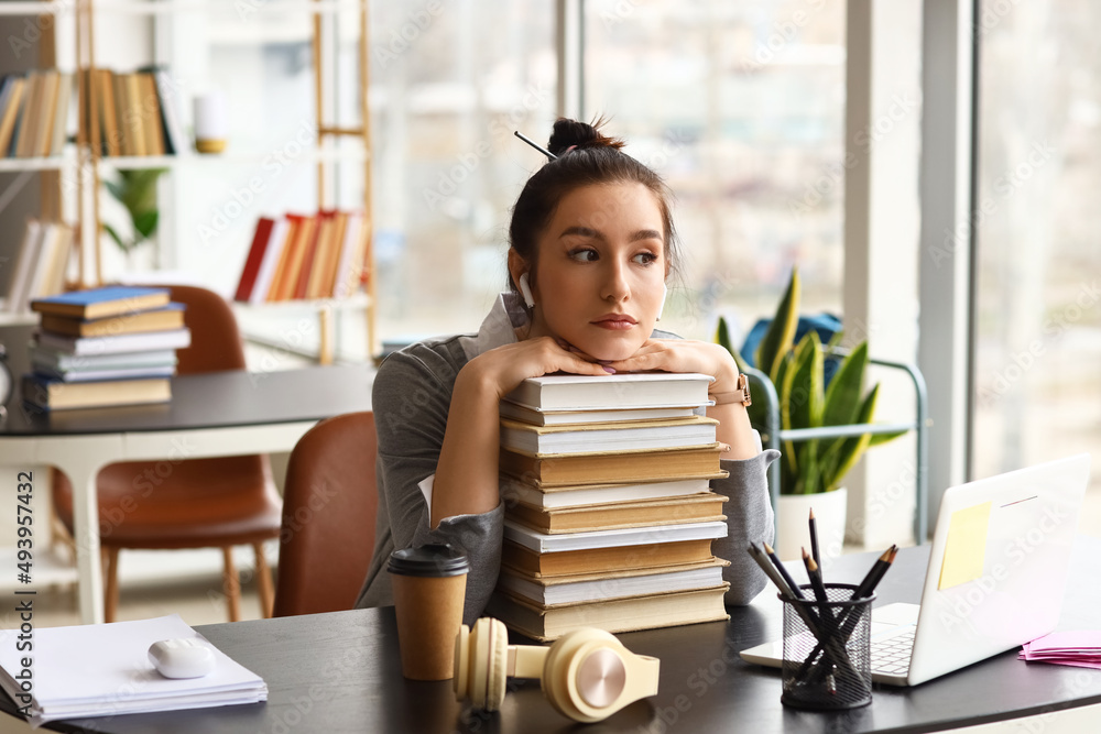 Beautiful female student with stack of books in library