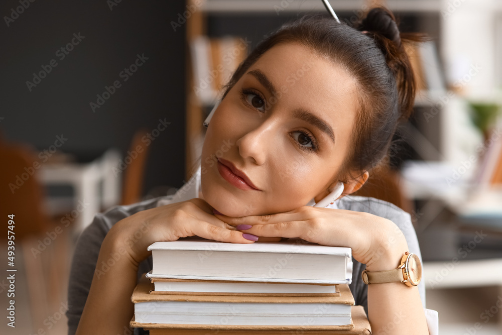 Beautiful female student with stack of books in library