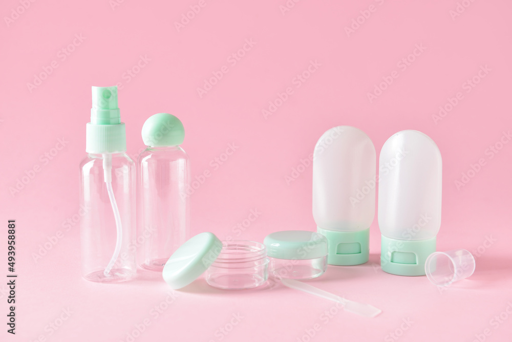 Set of empty travel cosmetic bottles and jars on pink background