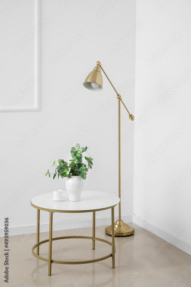 Modern table with houseplant and lamp in interior of light room