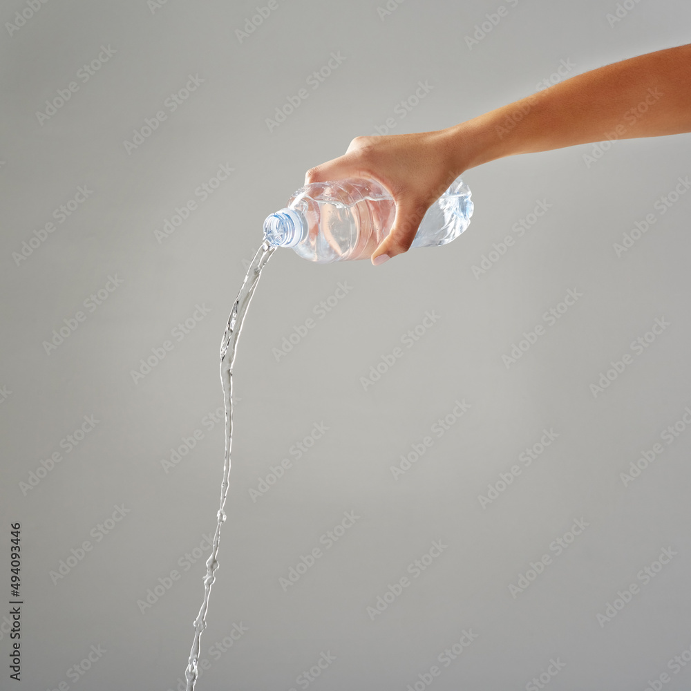 Purified water. Cropped shot of water being poured out of a bottle against a grey background.