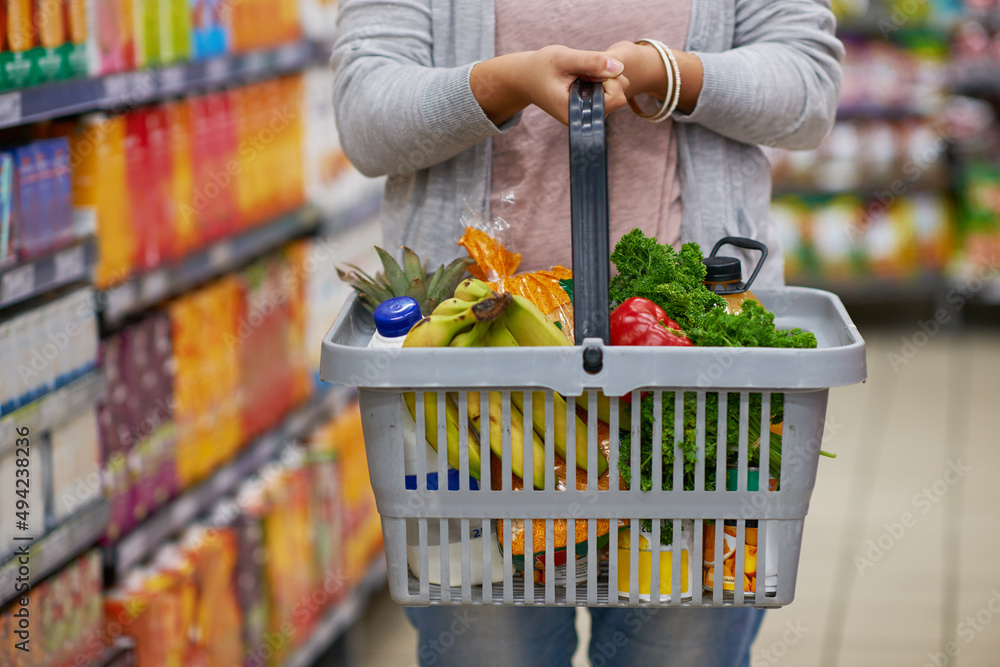 Filling up on some freshness. Closeup shot of a woman holding a basket full of groceries in a superm