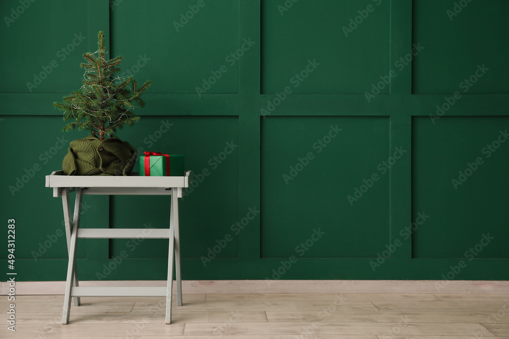 Interior of room with Christmas tree and gift box on table near color wall