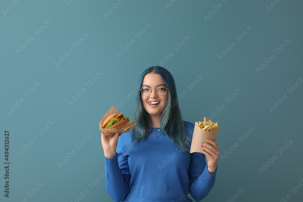 Young woman with unusual hair holding burger and french fries on color background