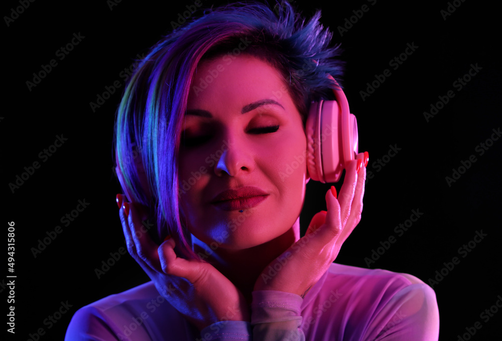 Beautiful woman with unusual hair listening to music on black background