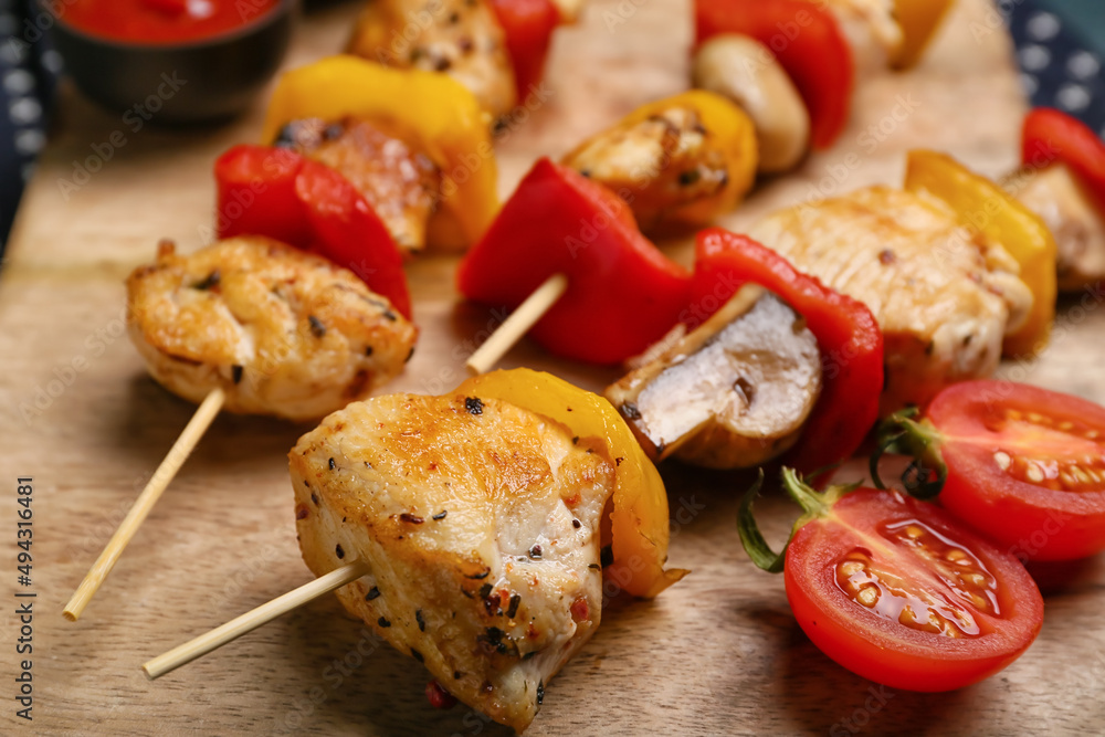 Wooden board of grilled chicken skewers with vegetables on table, closeup