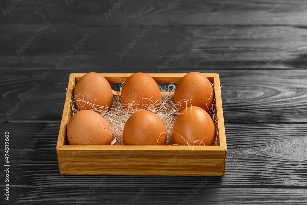 Box with fresh chicken eggs on black wooden background