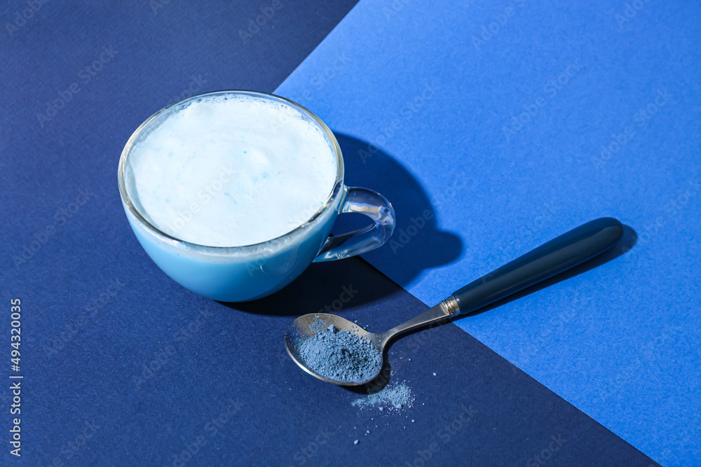 Cup of delicious matcha tea and spoon with powder on blue background