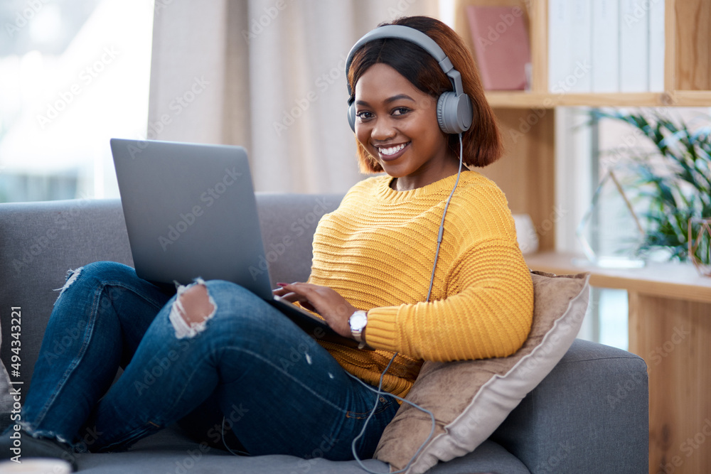 Home is my happy place. Shot of an attractive young woman wearing headphones while using her laptop.