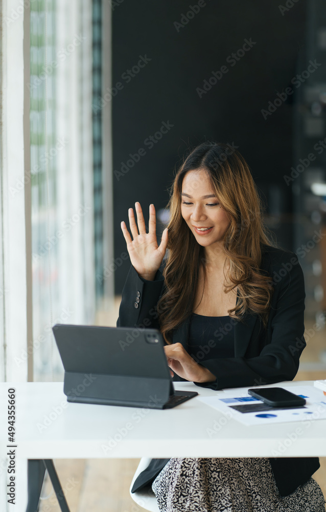 快乐的年轻女性坐在办公桌前，挥手问候同事。迷人的商务女性