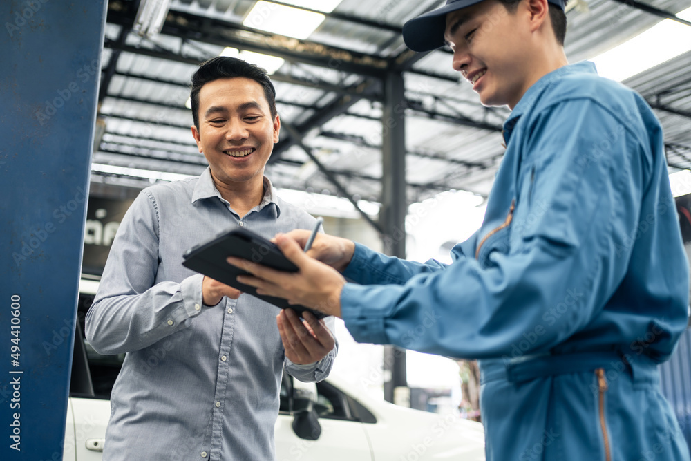 Asian automotive mechanic explain car condition to client in garage. 