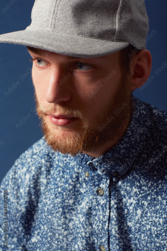 Thinking it over. A young man with a beard and unique sense of style looking away.