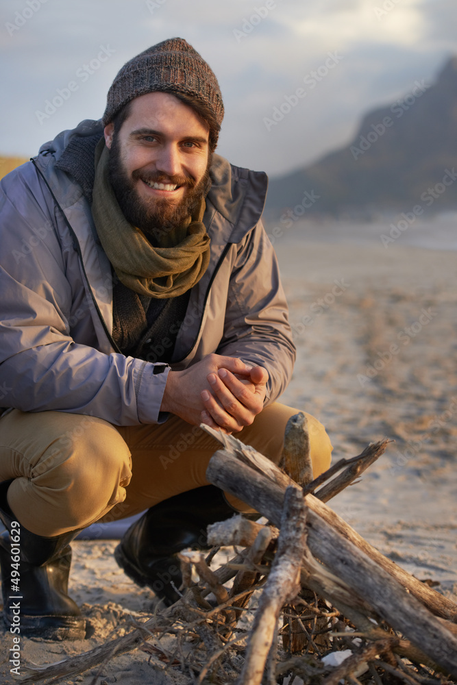 Itll get warm soon. A young man building a fire on the beach.