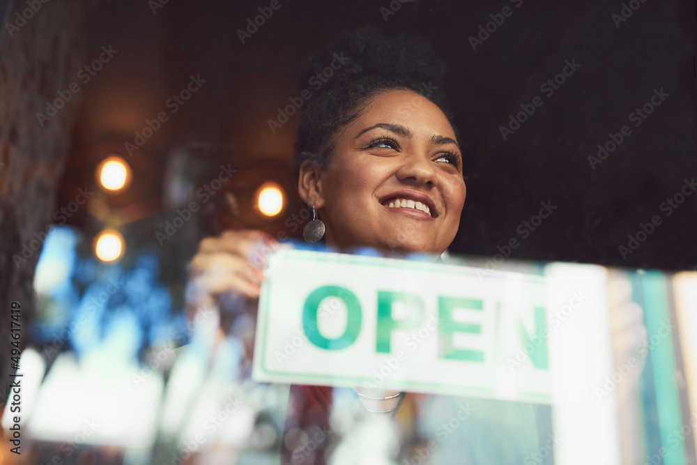 Customers will soon come flooding in. Cropped shot of a young woman hanging up an open sign on the w