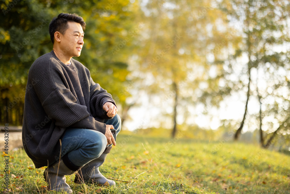 亚洲男子在湖岸休息的肖像。大自然中休闲、爱好和周末的概念。秋天