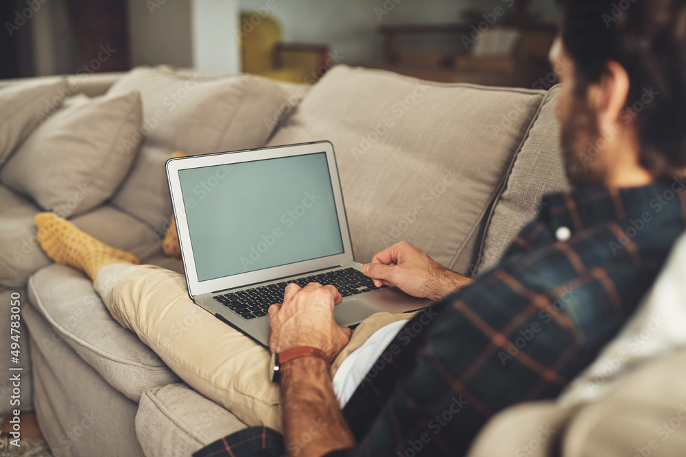 This is how I keep up with the world. Shot of a handsome young man using his laptop while relaxing o