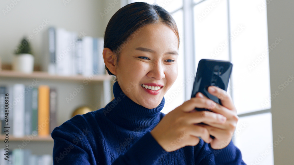 Young Asian woman with smile using smartphone for social media, shopping online, playing game at hom