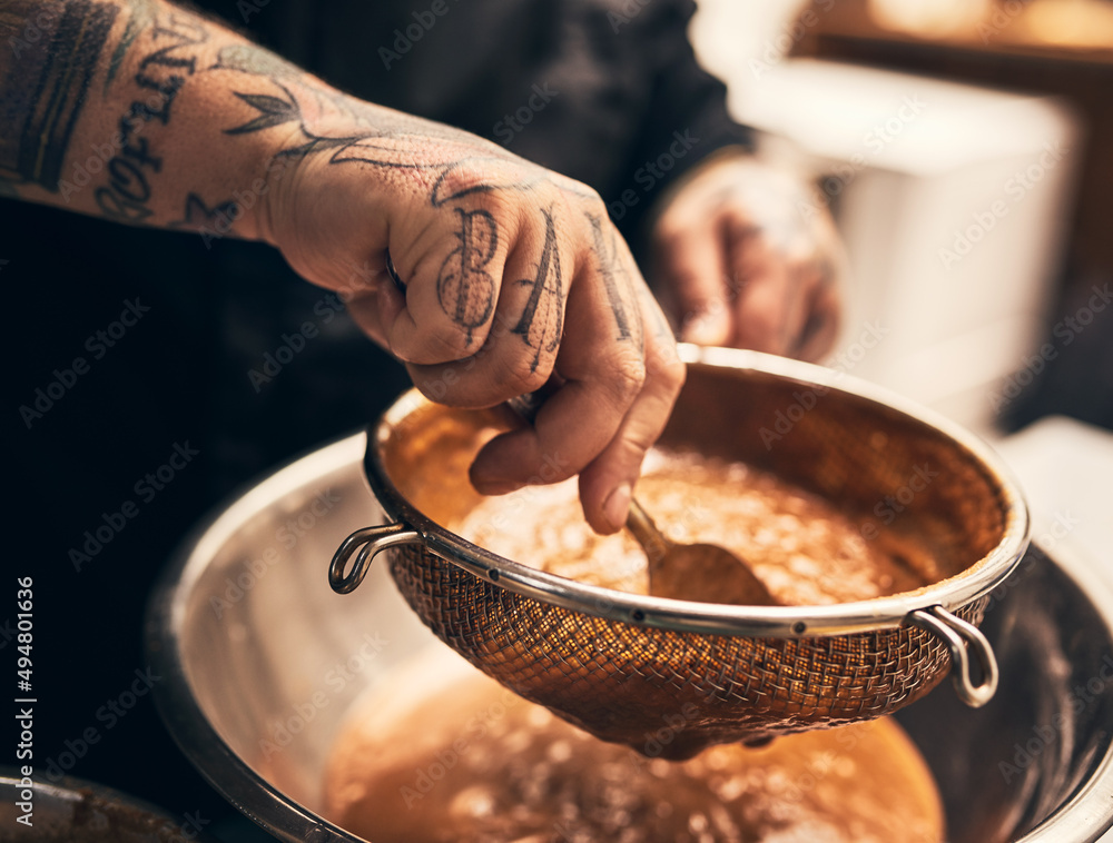 This dish is a knock out. Closeup of a unrecognisable chefs tattooed hands straining food into a bow