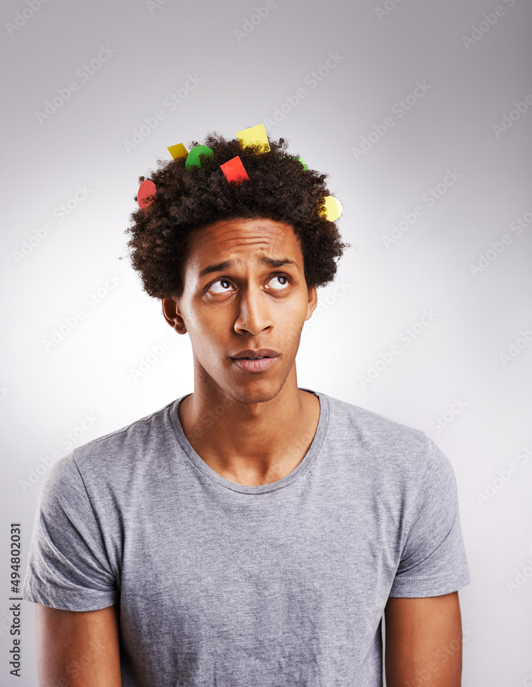 Its time to think in color. Shot of a young man with colorful paper in his hair against a gray backg