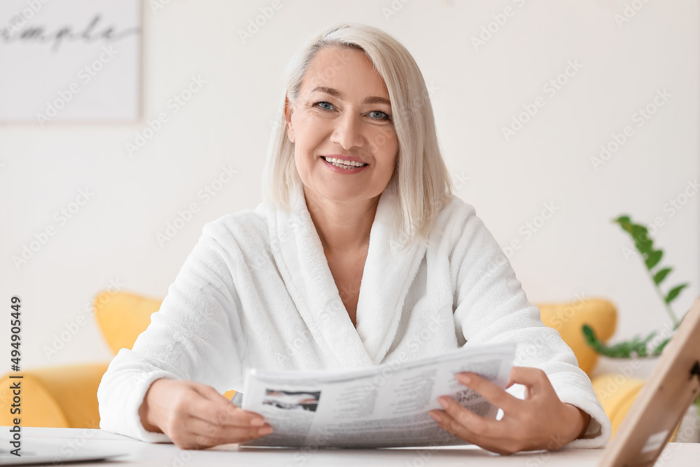 Beautiful mature woman reading newspaper at table