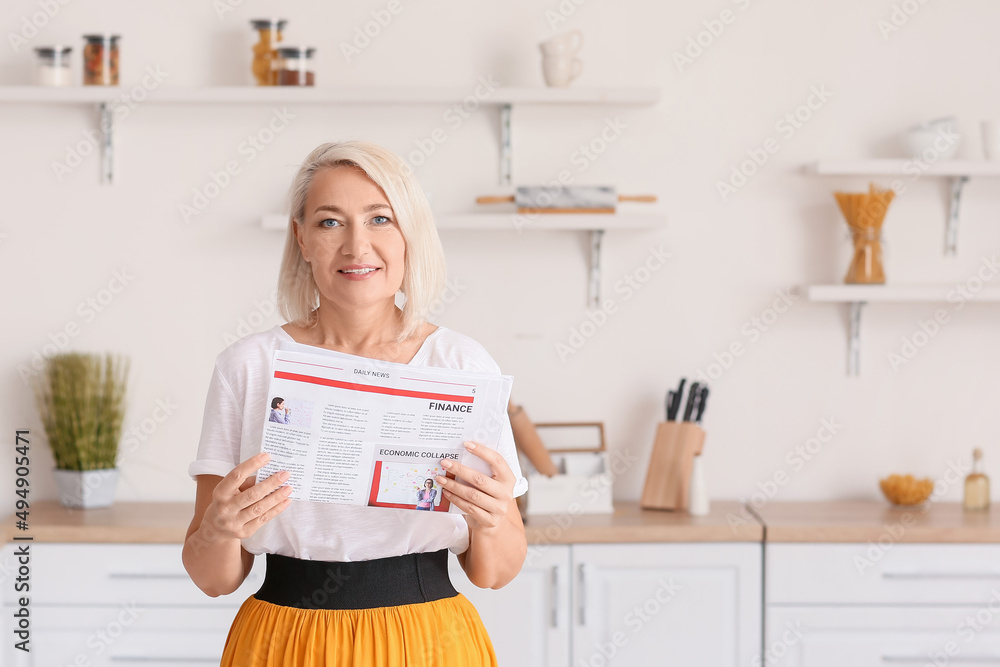 Beautiful mature woman reading newspaper in kitchen